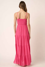 Back view of a woman wearing a hot pink maxi dress against a plain background