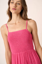 Woman wearing a hot pink smocked dress against a plain background