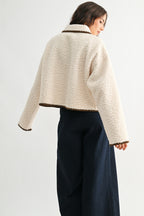 Back view of a woman wearing a cream sherpa jacket with dark brown trim and jeans on a white background 