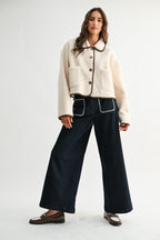 Woman wearing a cream sherpa jacket with dark brown trim and jeans on a white background 