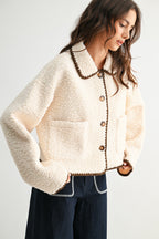 Woman wearing a cream sherpa jacket with dark brown trim and jeans on a white background 