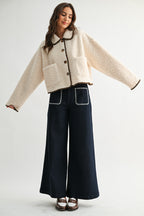 Woman wearing a cream sherpa jacket with dark brown trim and jeans on a white background 