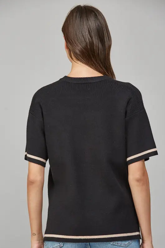 Back view of a woman wearing a black short-sleeve sweater with tan trim on a gray background