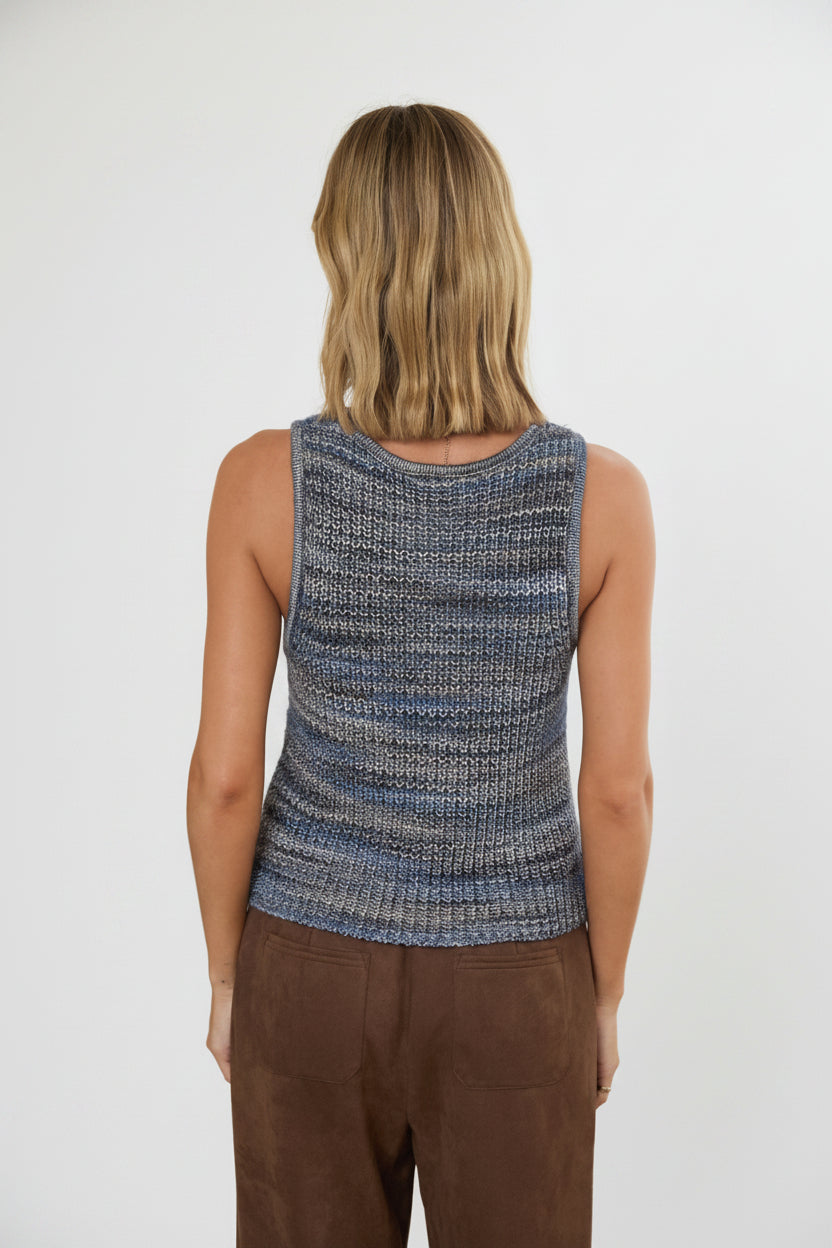 Back view of a woman wearing a blue multi knitted sleeveless tank top in a bright room.