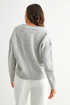 Back view of a woman wearing a heather grey knit sweater against a white background