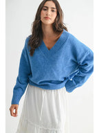 Woman wearing a blue V-neck sweater and white skirt against a white background