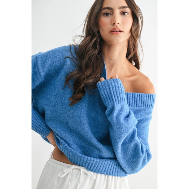 Woman wearing a blue V-neck sweater and white skirt against a white background
