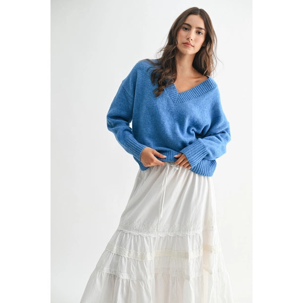 Woman wearing a blue V-neck sweater and white skirt against a white background