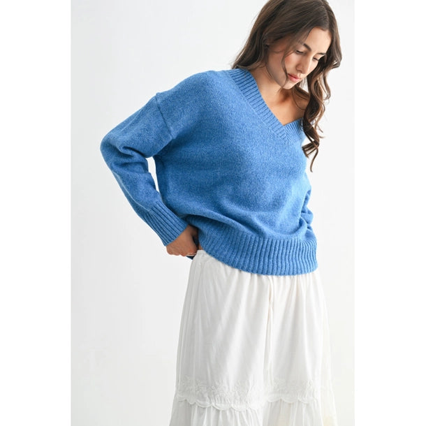 Woman wearing a blue V-neck sweater and white skirt against a white background