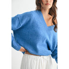 Woman wearing a blue V-neck sweater and white skirt against a white background