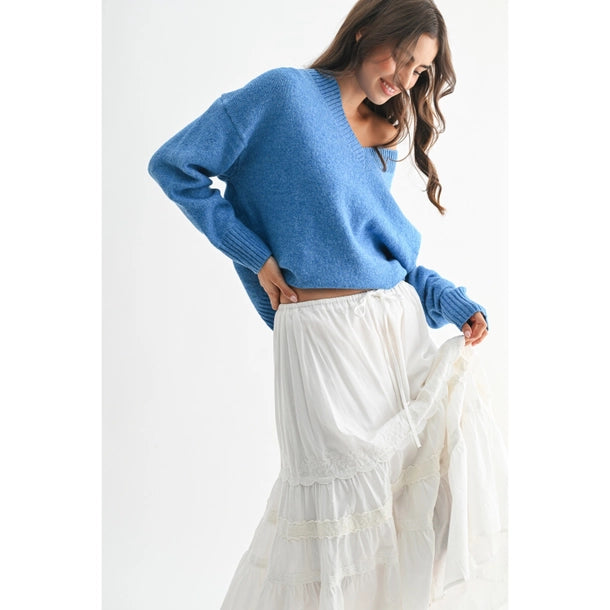 Woman wearing a blue V-neck sweater and white skirt against a white background