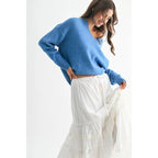 Woman wearing a blue V-neck sweater and white skirt against a white background