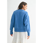 Back view of a woman wearing a blue V-neck sweater and white skirt against a white background