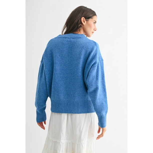 Back view of a woman wearing a blue V-neck sweater and white skirt against a white background