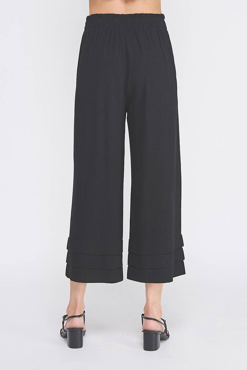 Back view of black linen blend wide-leg pants worn by a woman on a white background