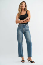 Woman wearing a black tank top and high rise straight leg medium blue jeans on a white background