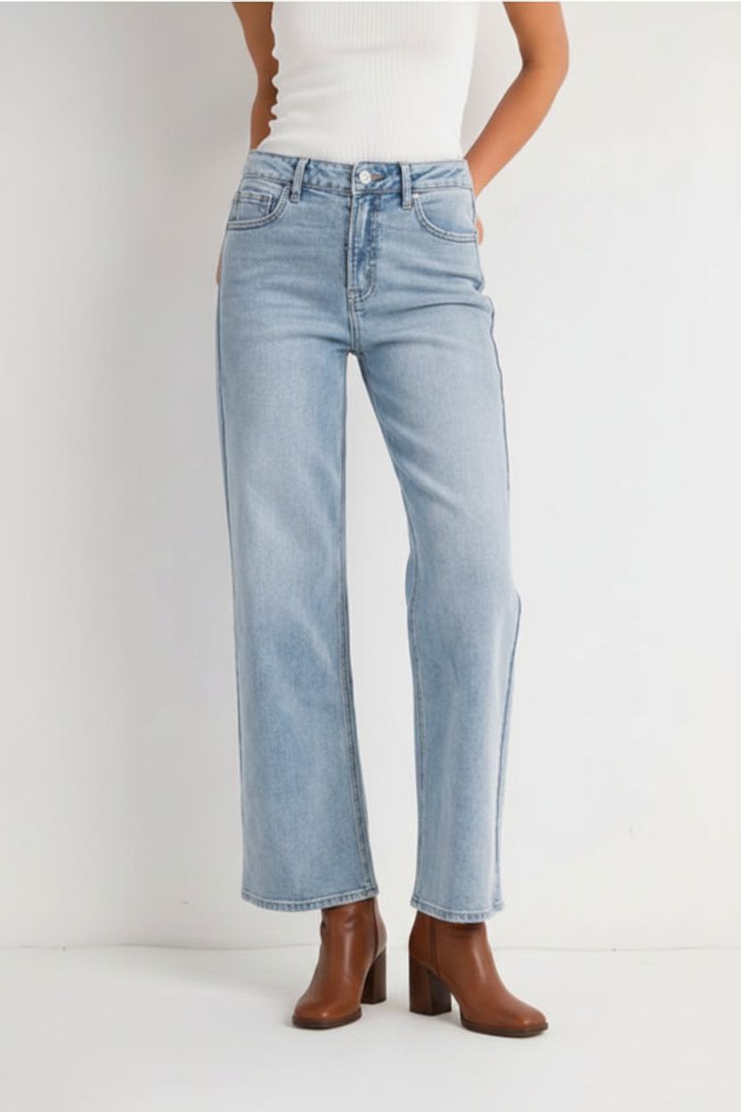A model from the waist down wearing light-wash blue straight-leg jeans, a white ribbed top, and brown heeled ankle boots, standing against a plain white studio background.