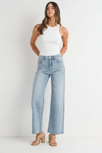 Woman wearing a white tank top and light blue high right straight leg jeans against a white background