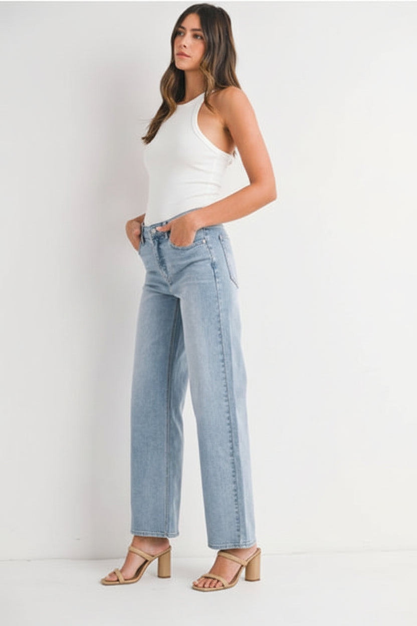 Woman wearing a white tank top and light blue high right straight leg jeans against a white background
