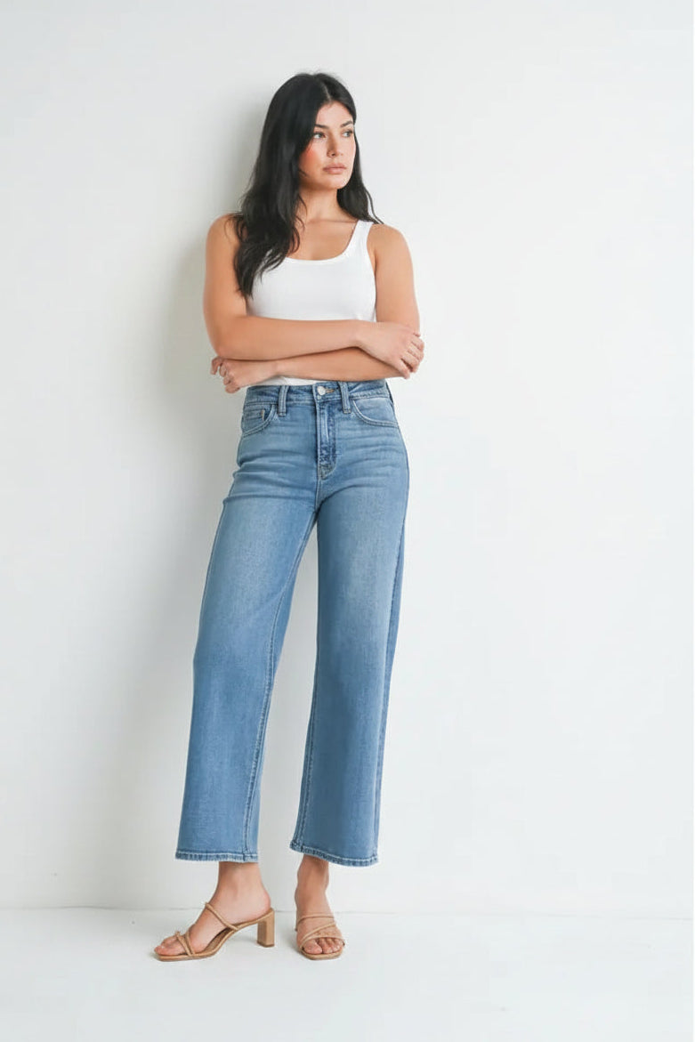 Woman wearing light blue denim high rise slim wide leg jeans and white top on a white background