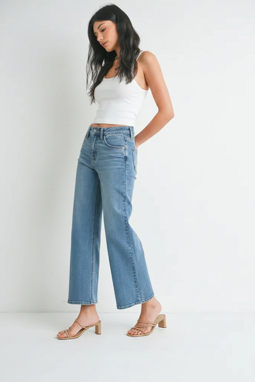 Woman wearing light blue denim high rise slim wide leg jeans and white top on a white background