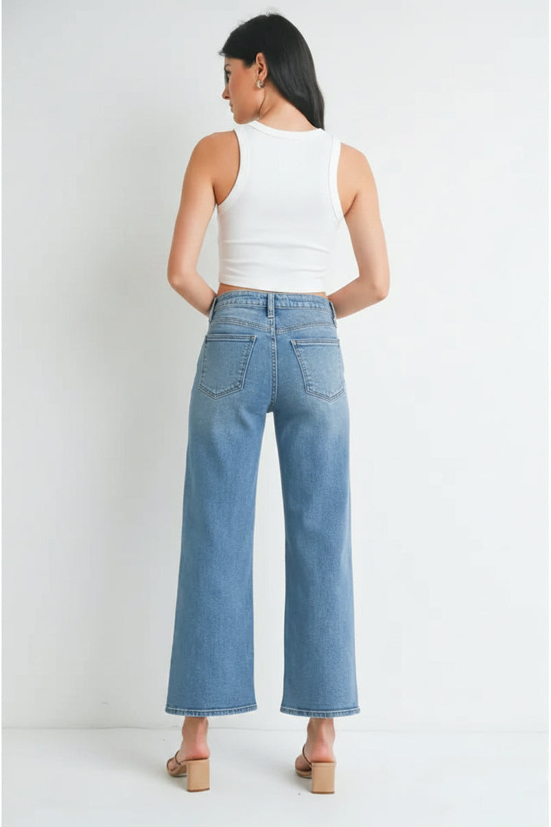 Back view of a woman wearing light blue denim high rise slim wide leg jeans and white top on a white background
