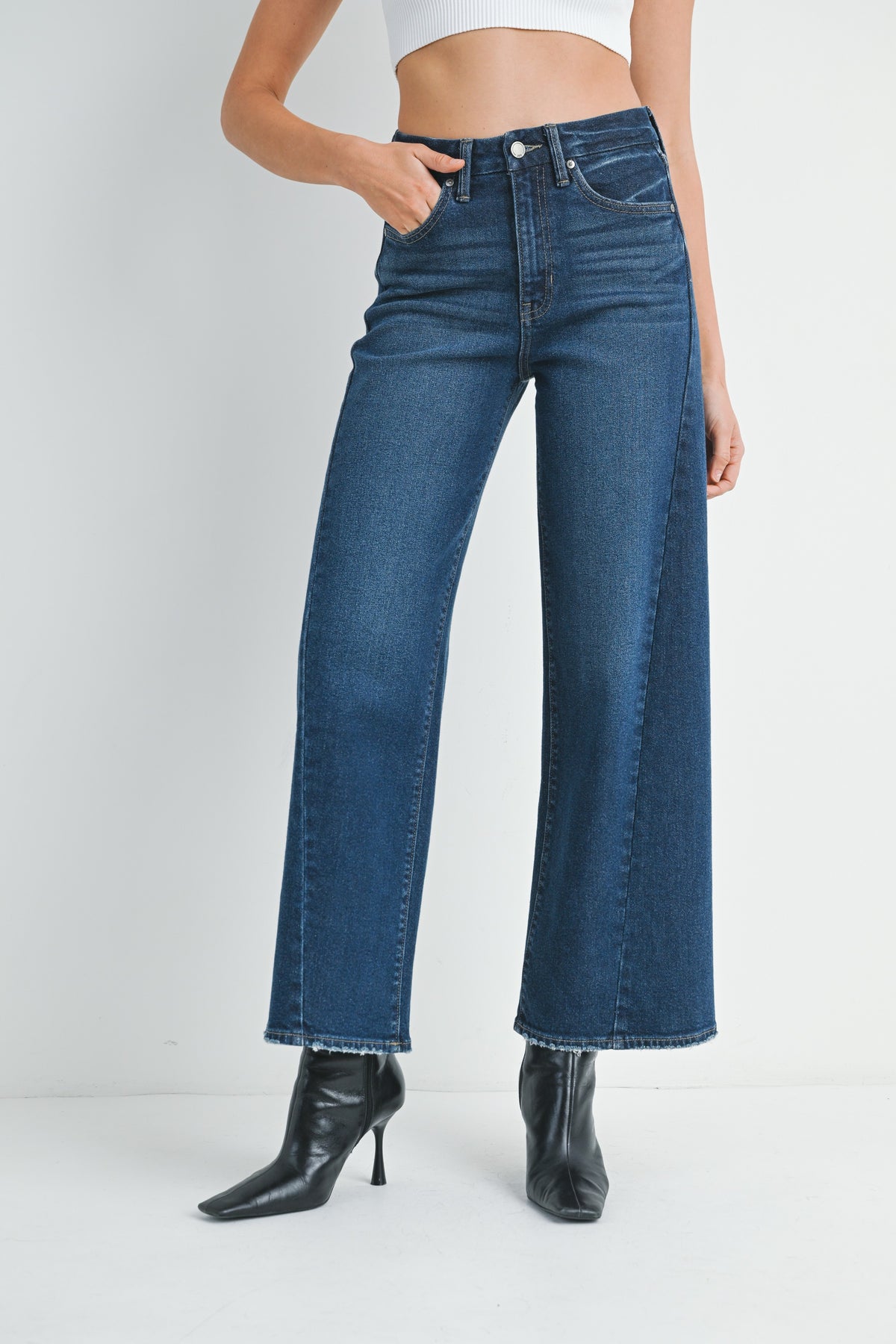 Woman wearing barrel leg dark denim jeans and black high-heeled shoes on a white background