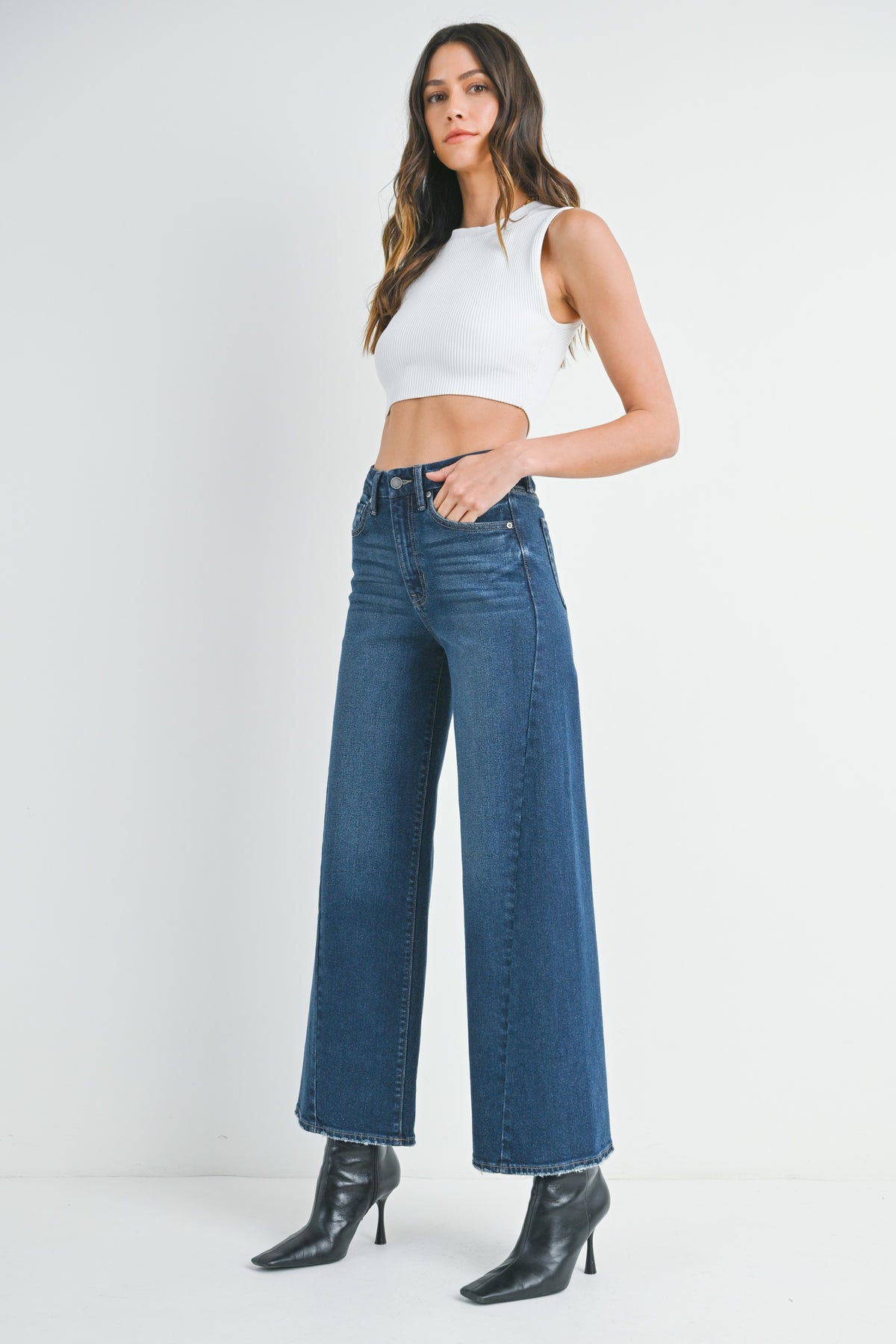 Woman wearing barrel leg dark denim jeans, white top and black high-heeled shoes on a white background