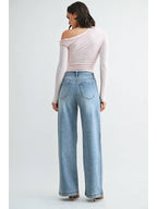 Back view of a woman wearing a light pink off-the-shoulder long-sleeve top and medium blue wide-leg jeans against a plain light gray studio background.