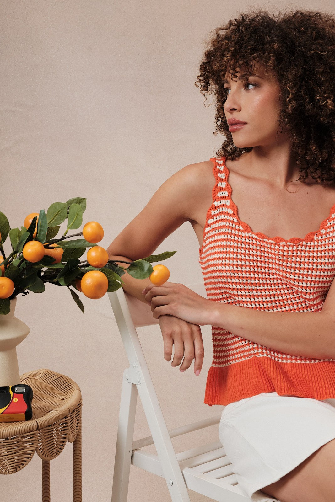 Woman wearing an orange and white  striped crochet knit tank top against a beige background