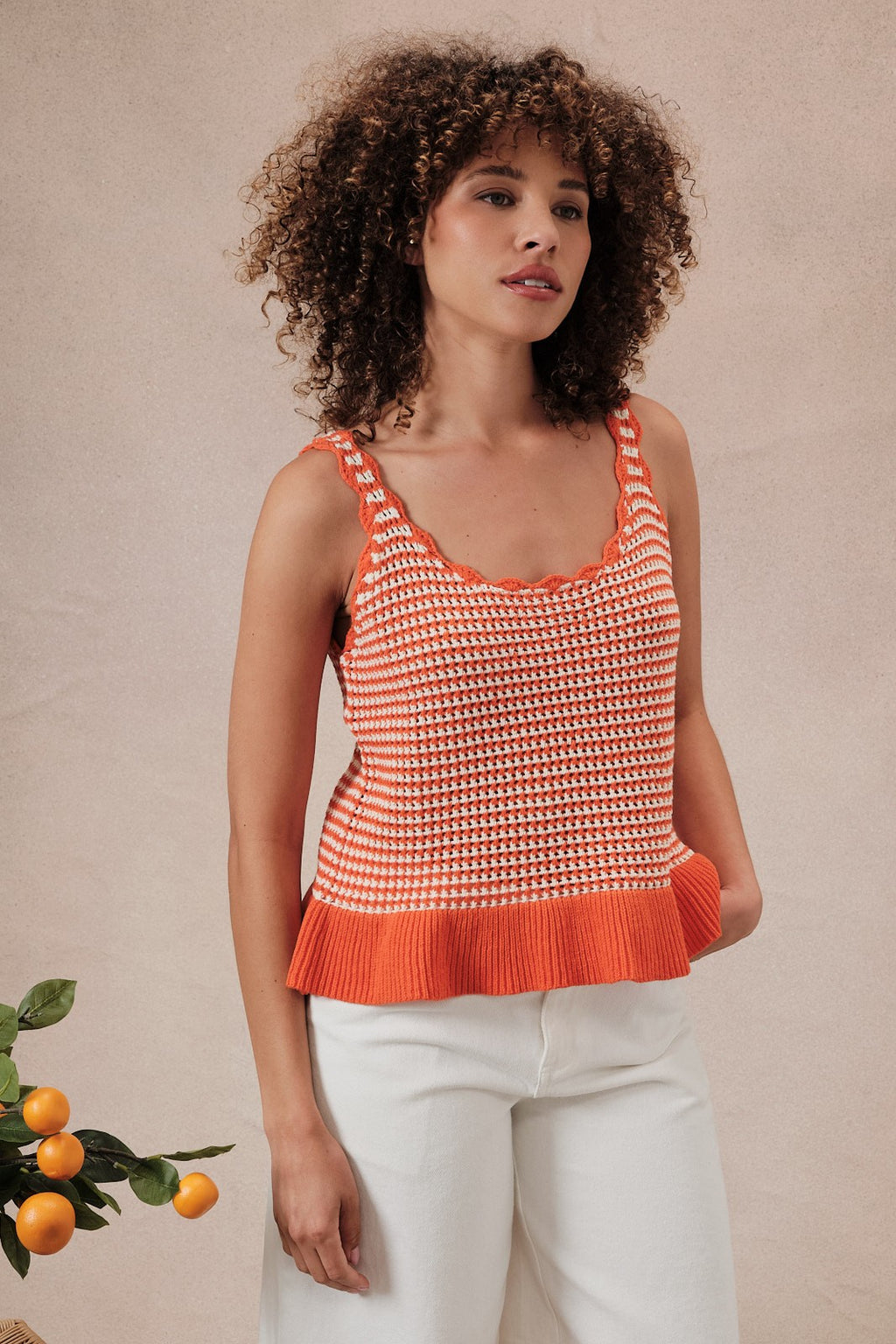 Woman wearing an orange and white  striped crochet knit tank top against a beige background