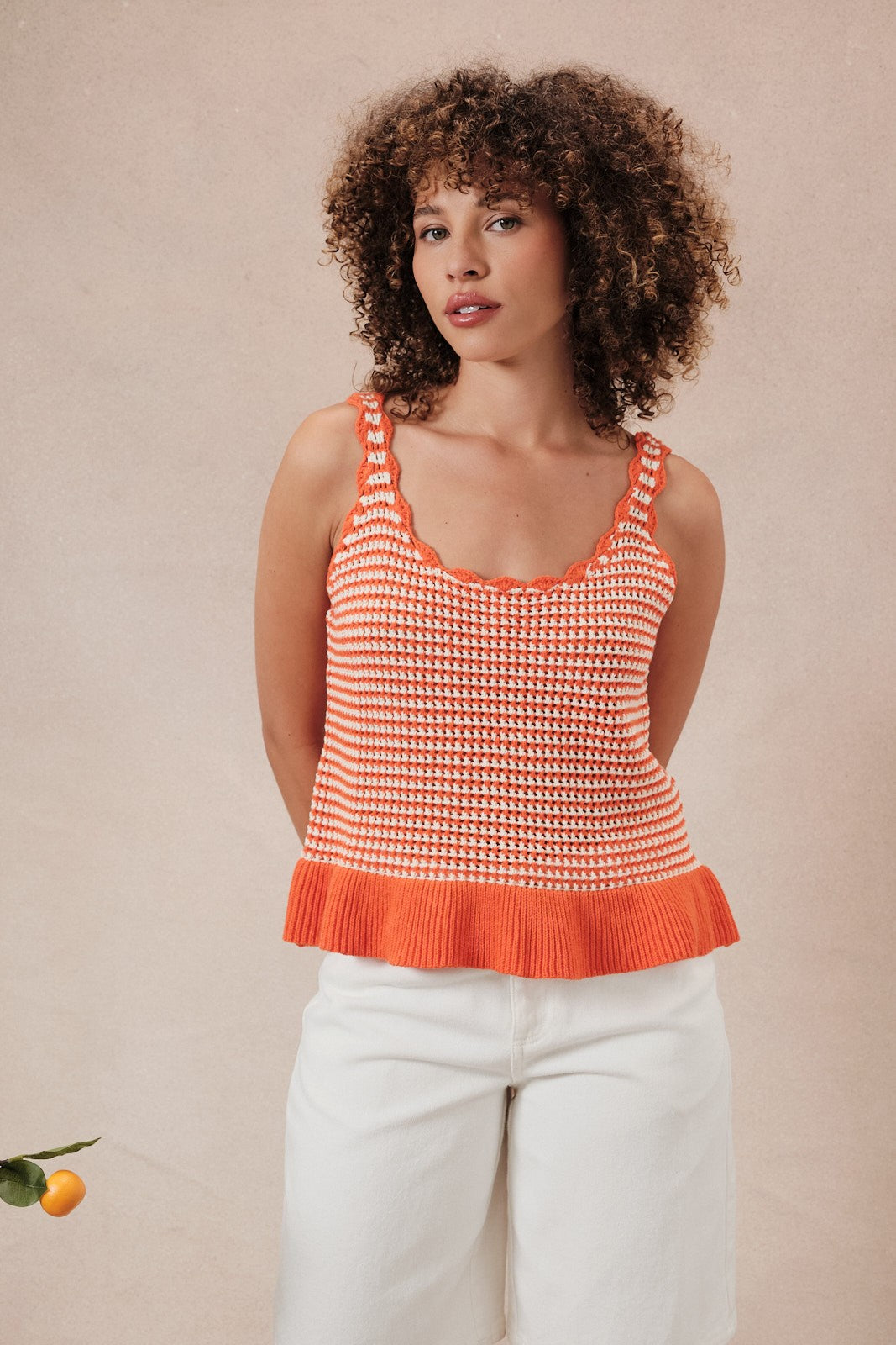 Woman wearing an orange and white  striped crochet knit tank top against a beige background