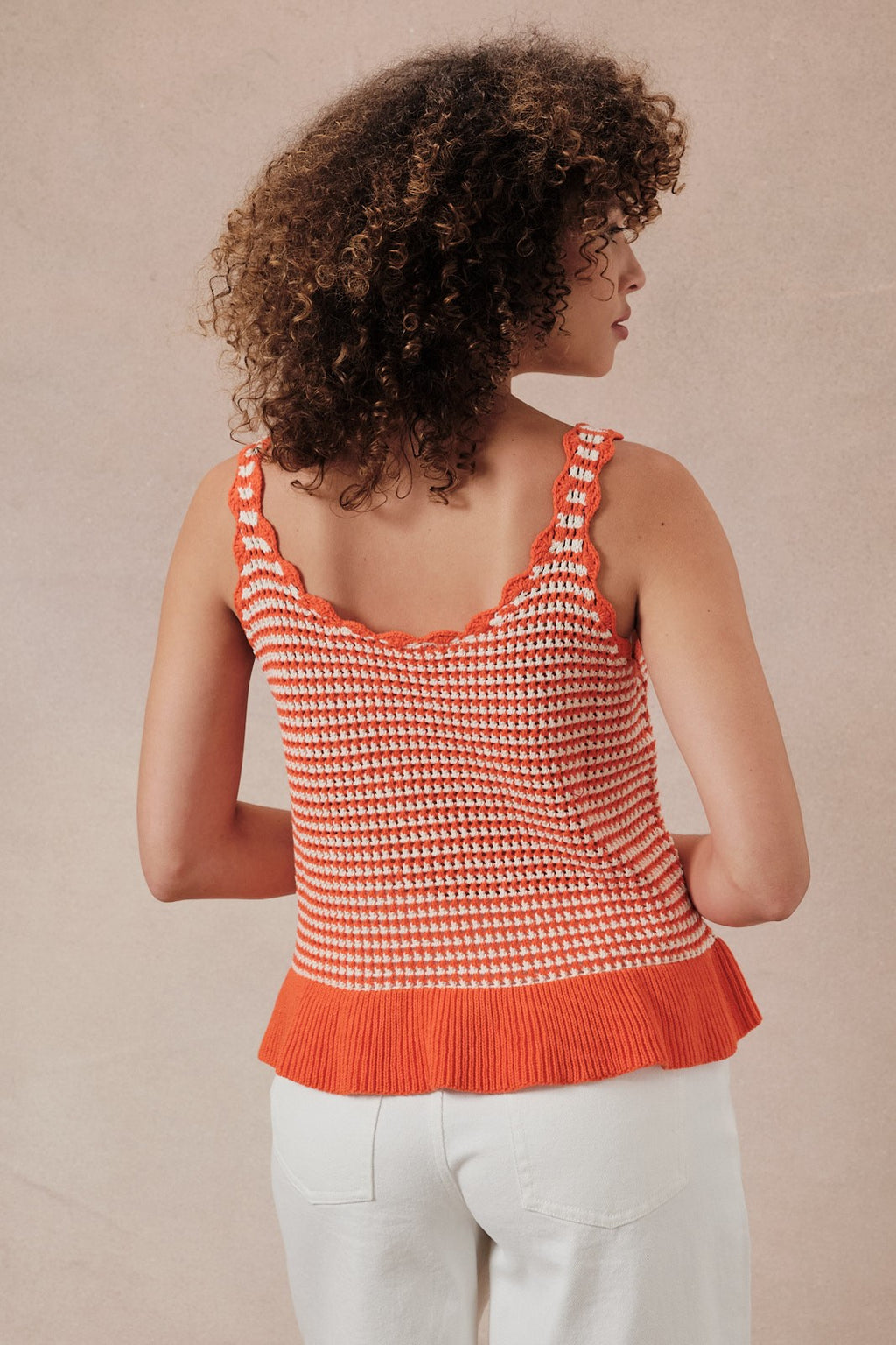 Back view of a woman wearing an orange and white  striped crochet knit tank top against a beige background