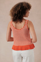 Back view of a woman wearing an orange and white  striped crochet knit tank top against a beige background