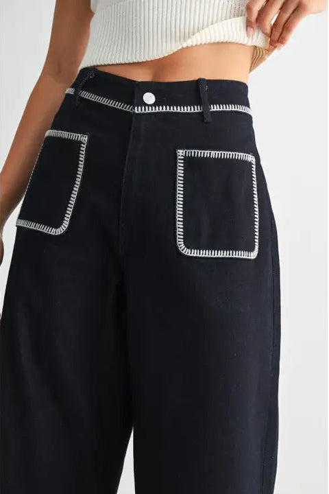 Women's dark denim pants with white stitching on a plain background