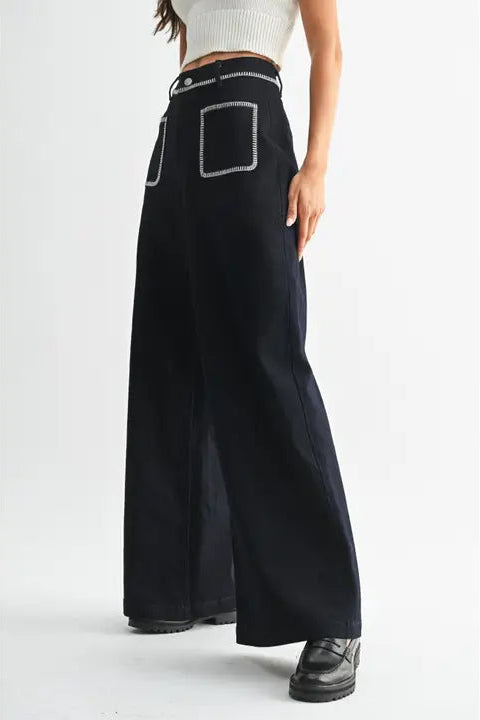 Woman wearing dark denim wide-leg pants with white accents on a white background