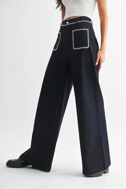 Women's dark denim wide-leg pants with white accents worn by a person on a white background