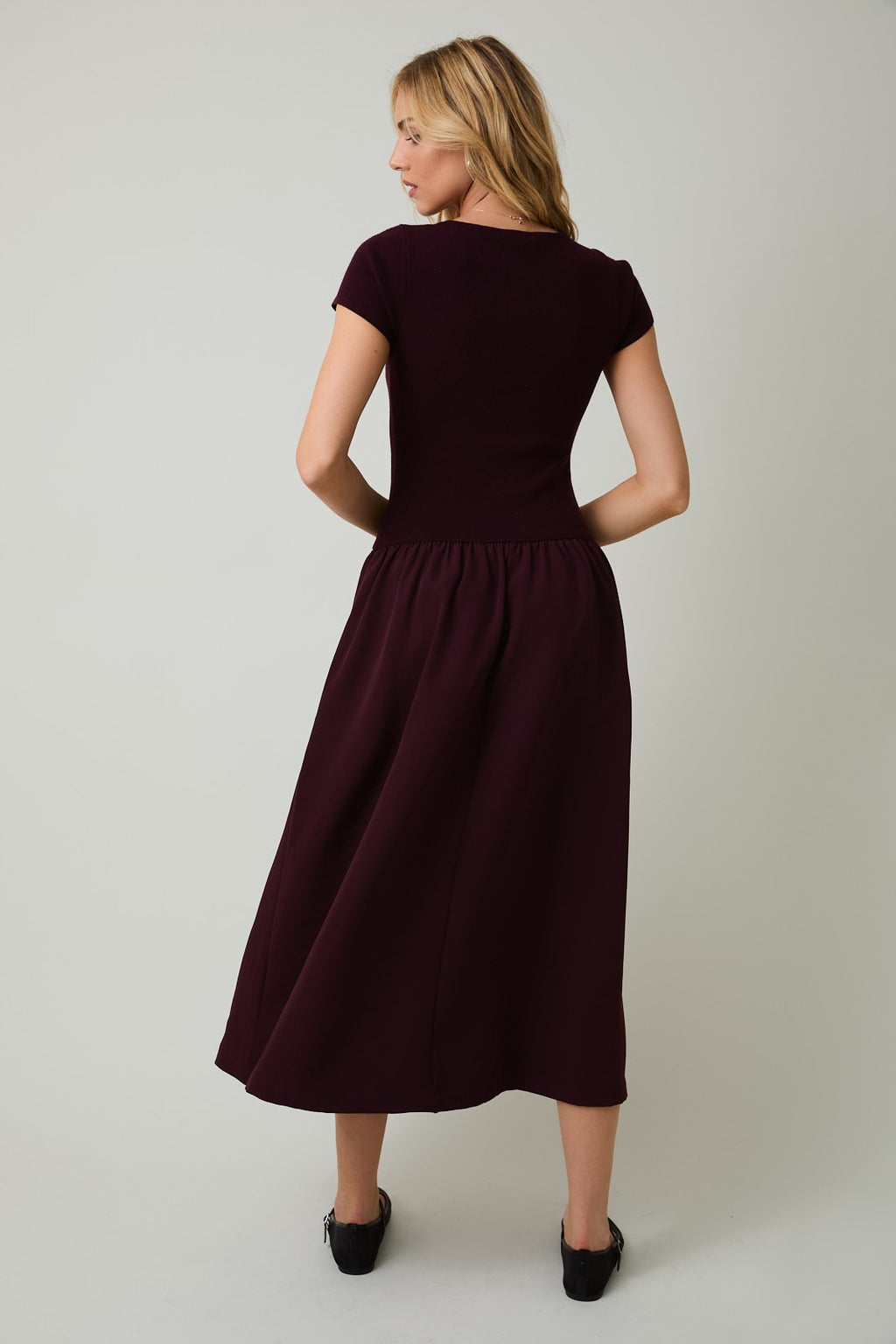 Back view of a woman wearing a plum midi dress against a plain background