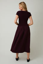Back view of a woman wearing a plum midi dress against a plain background