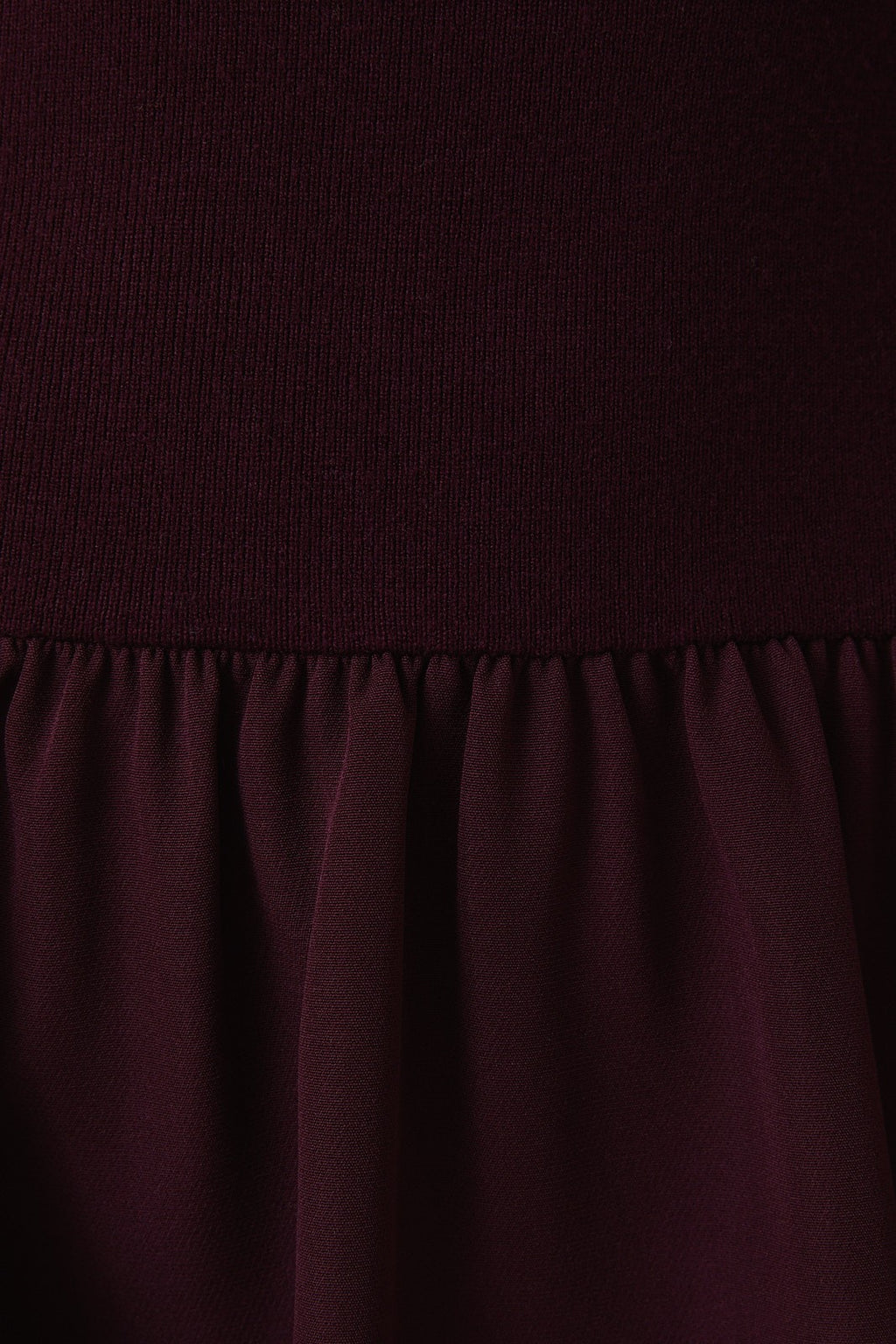 Close-up of a plum knit top and woven fabric skirt with matte satin texture.