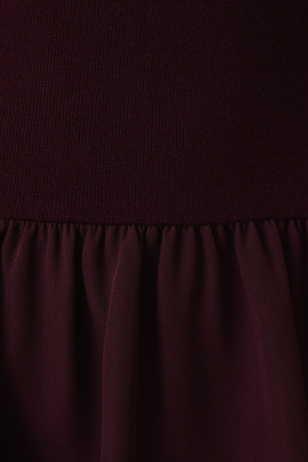 Close-up of a plum knit top and woven fabric skirt with matte satin texture.