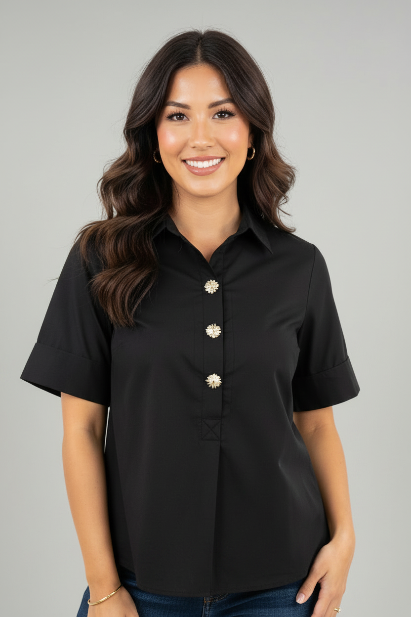 A woman modeling a black short sleeve blouse with gold tone buttons and front pleat against a white background.