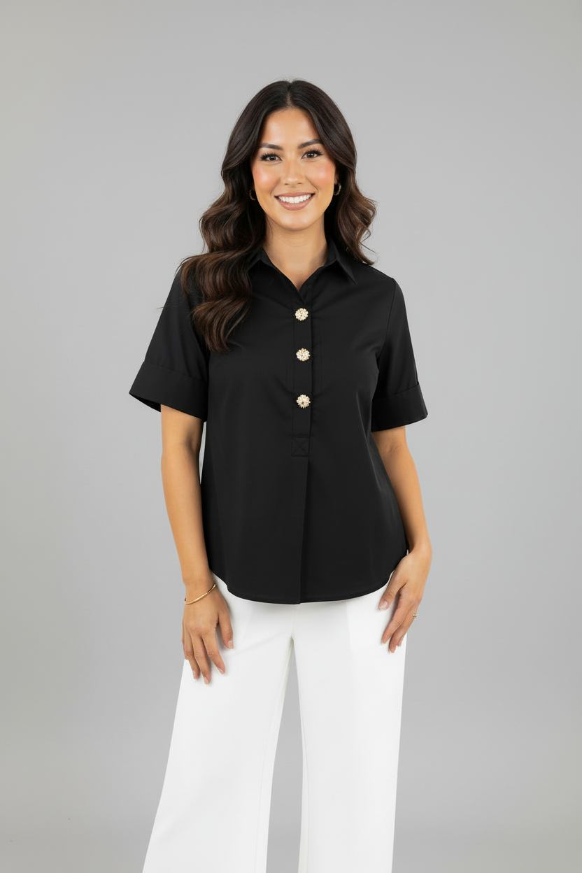 A woman modeling a black short sleeve blouse with gold tone buttons and front pleat and white pants against a gray background.