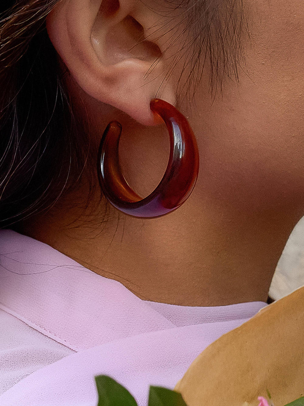 Close-up of a woman wearing a brown resin hoop earring.