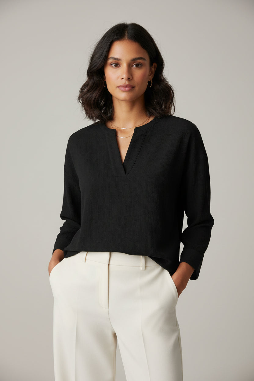 Woman wearing a black long sleeve textured top with white pants against a plain background