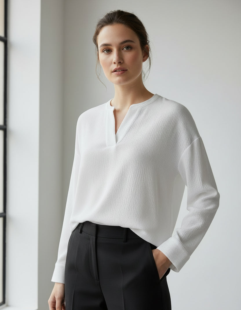 Woman wearing a white textured long sleeve top and black pants against a neutral background