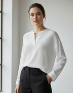 Woman wearing a white textured long sleeve top and black pants against a neutral background