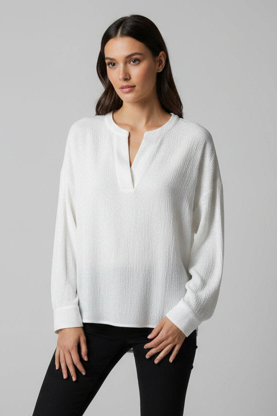 Woman wearing a white long sleeve textured top with black pants against a gray background