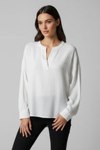 Woman wearing a white long sleeve textured top with black pants against a gray background