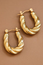 Pair of gold twisted hoop earrings on a brown background